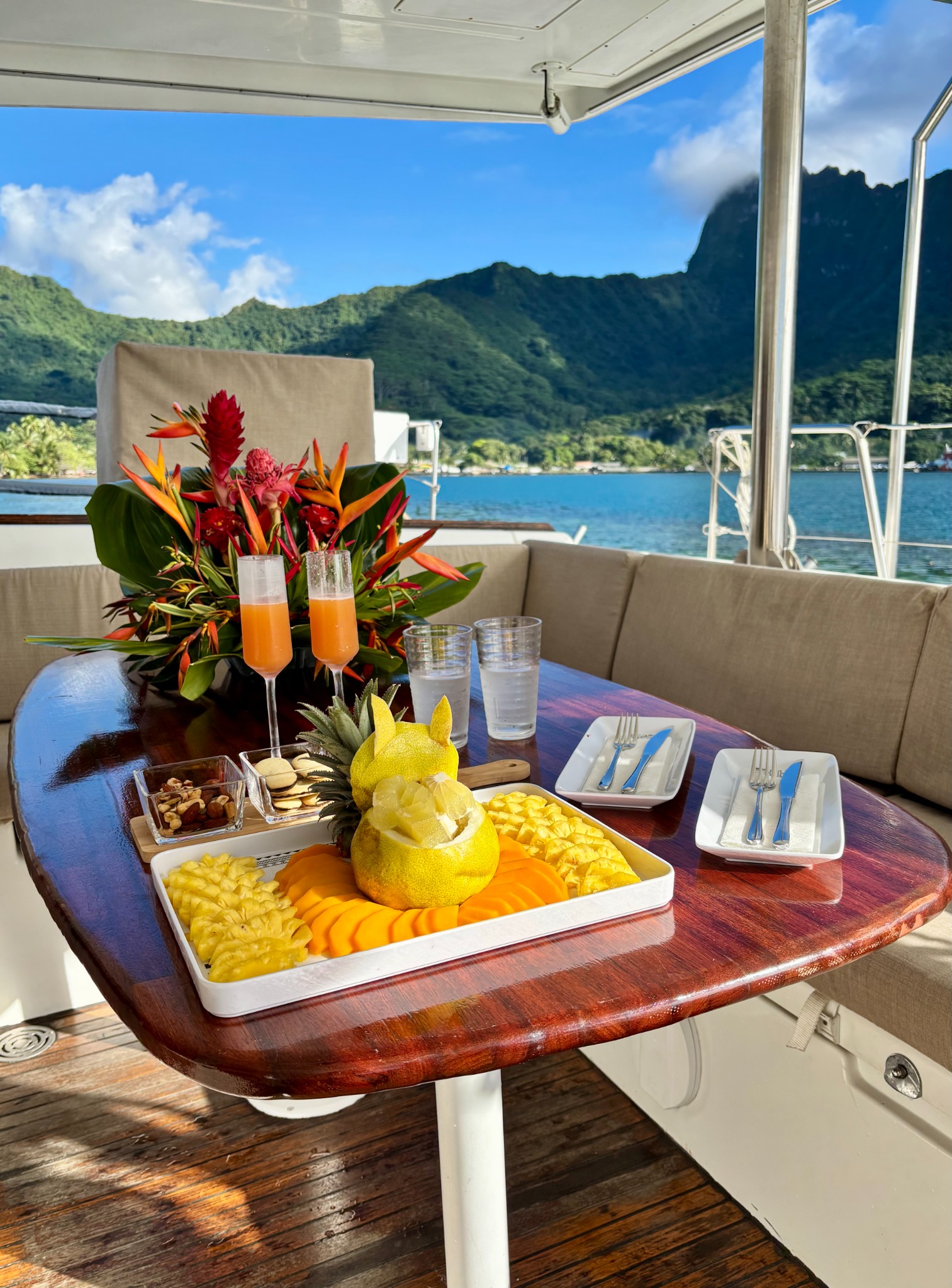 Punch de bienvenue et fruits tropicaux frais sur la table du catamaran, face aux montagnes de Moorea